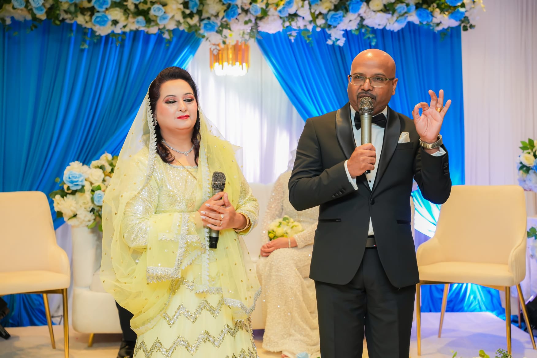 Pastor Haroon Angel preaching with a microphone beside a woman holding a microphone on stage